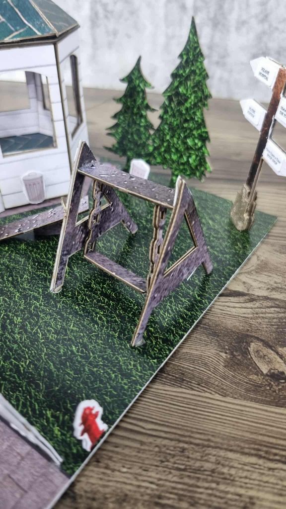 Miniature rotunda scene with porch bin, swing set, pine trees, and directional signpost in a grassy outdoor setting.