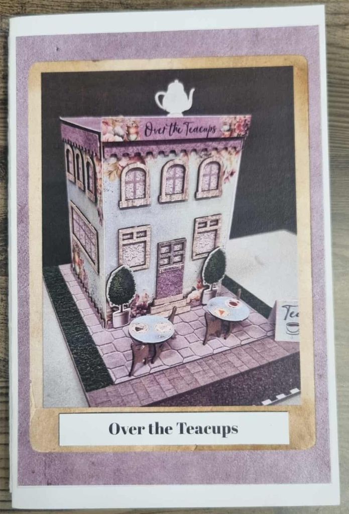 Miniature tea shop scene titled “Over the Teacups” with floral decor, outdoor tables, and teapot signage. One of the other buildings on 3Quarter Lane.
